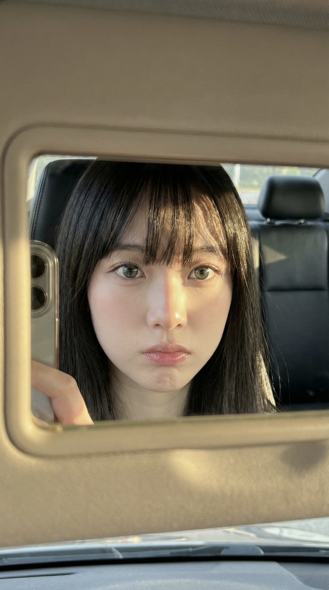 Extreme close-up of a young woman in a car, reflecting in a sun visor mirror, highlighting her soft oval face and natural skin texture.