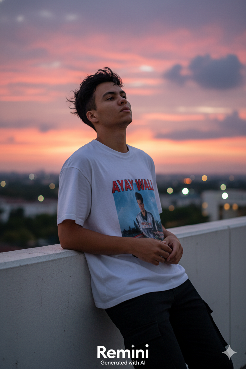 A close-up of a relaxed male model leaning against a white concrete wall during sunset, wearing an oversized white graphic t-shirt.