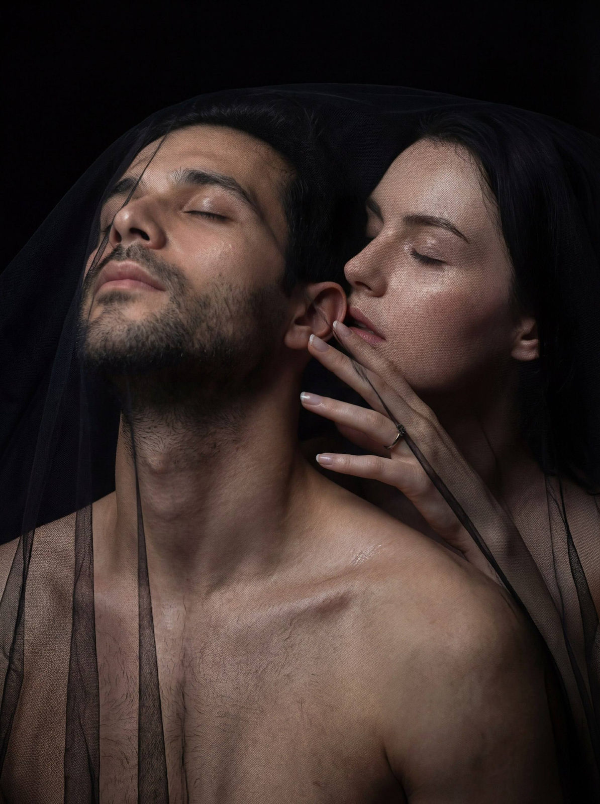 Close-up of a serene couple wrapped in a tulle veil, showcasing soft lighting and intimate expressions.