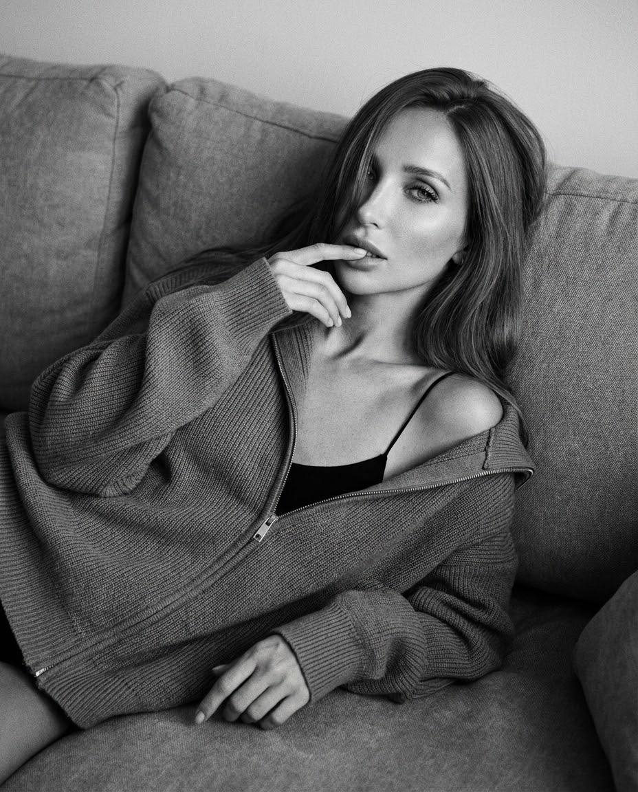 A woman reclining on a voluminous sofa, wearing an oversized sweater, with long hair falling over her face, evoking a sense of calm.