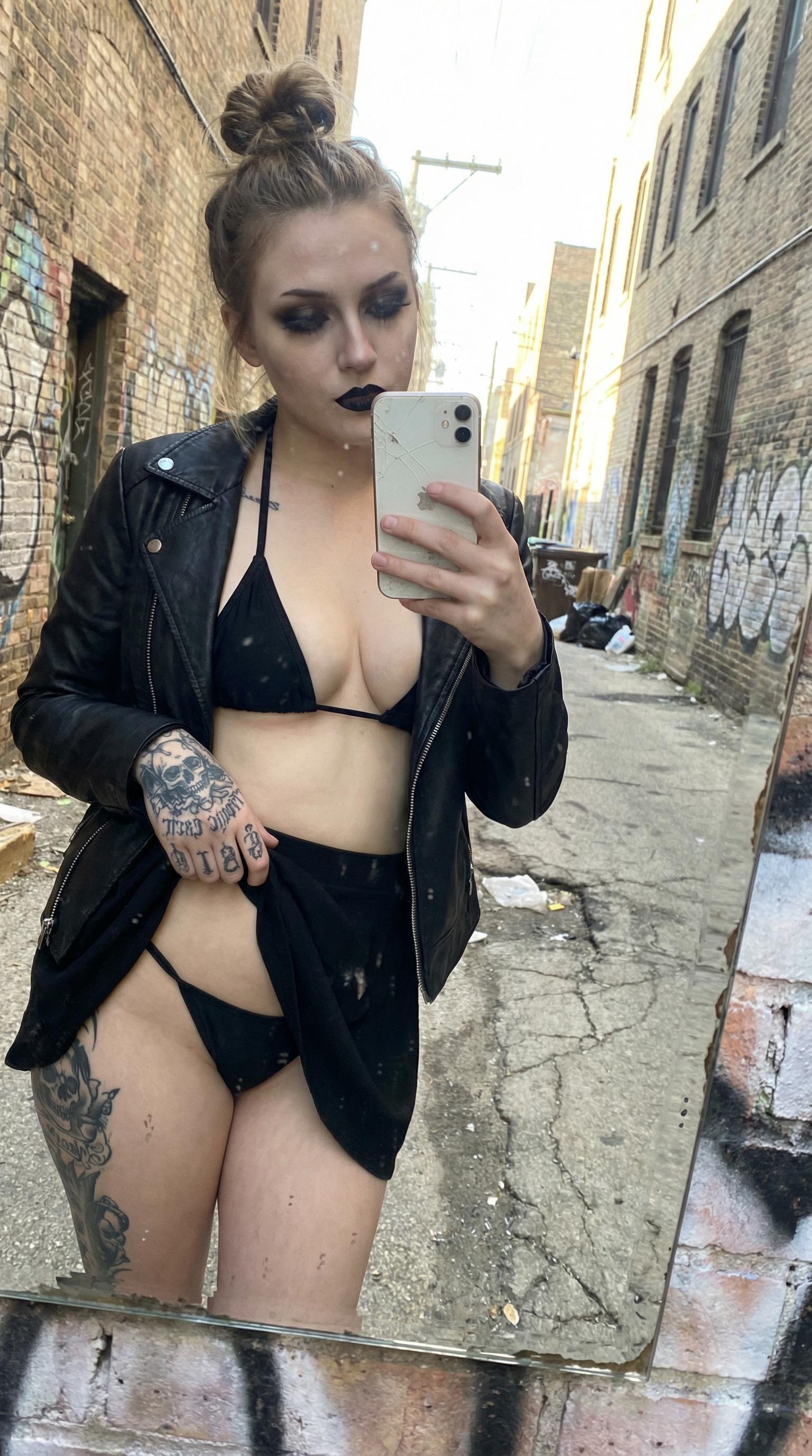 A woman taking a mirror selfie in a colorful graffiti alley, showcasing a casual seductive pose with a smartphone.