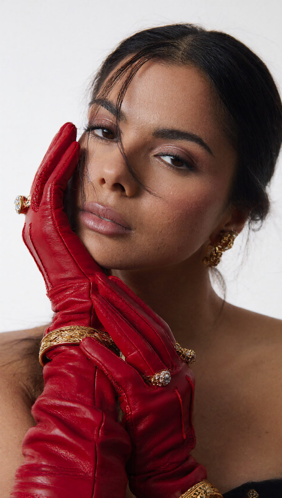 Intimate close-up of a woman with red leather gloves framing her face, capturing soft light and skin details.
