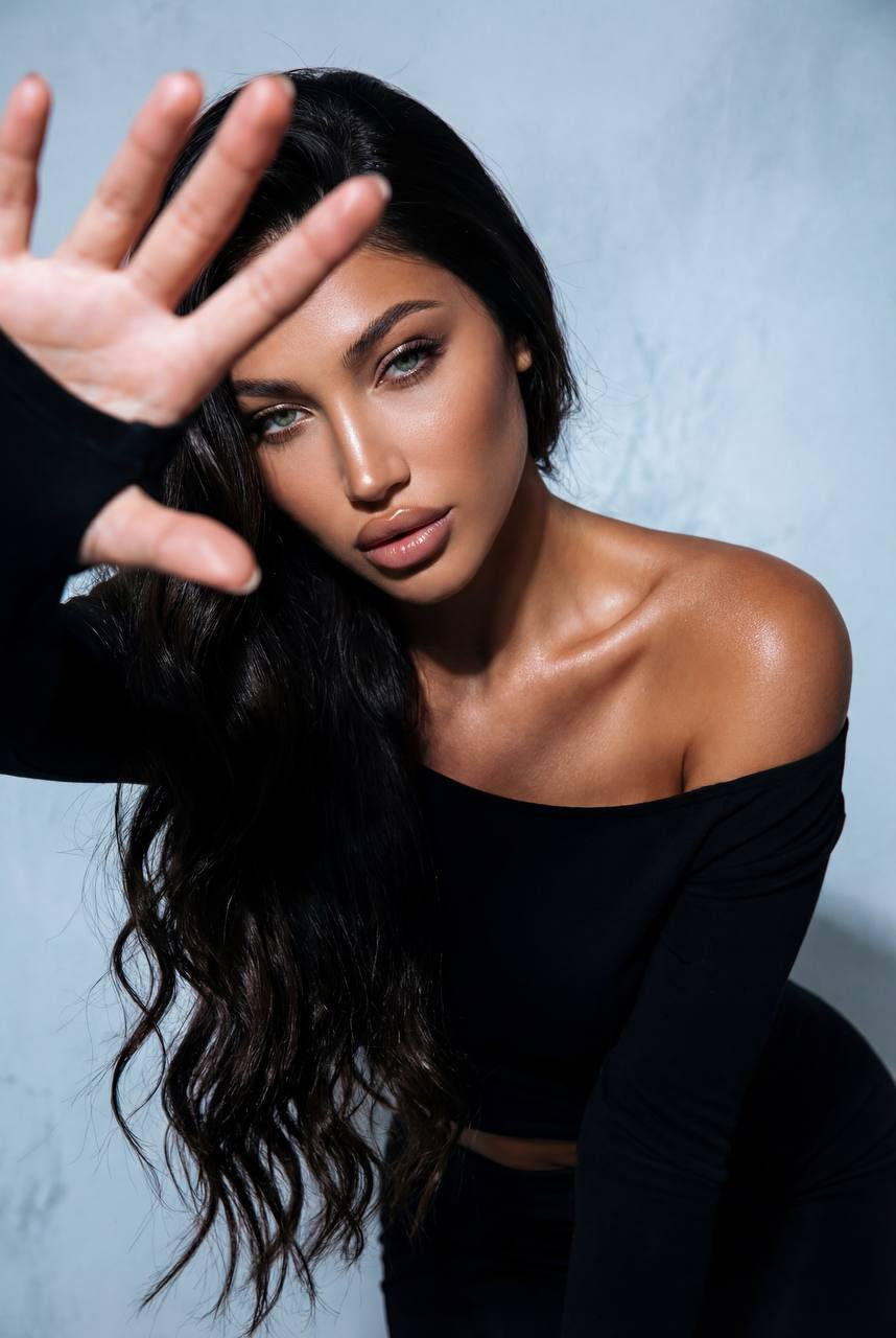 Dramatic editorial portrait of a woman leaning toward the camera, showcasing seductive expression and bold makeup in a minimal off-shoulder top.