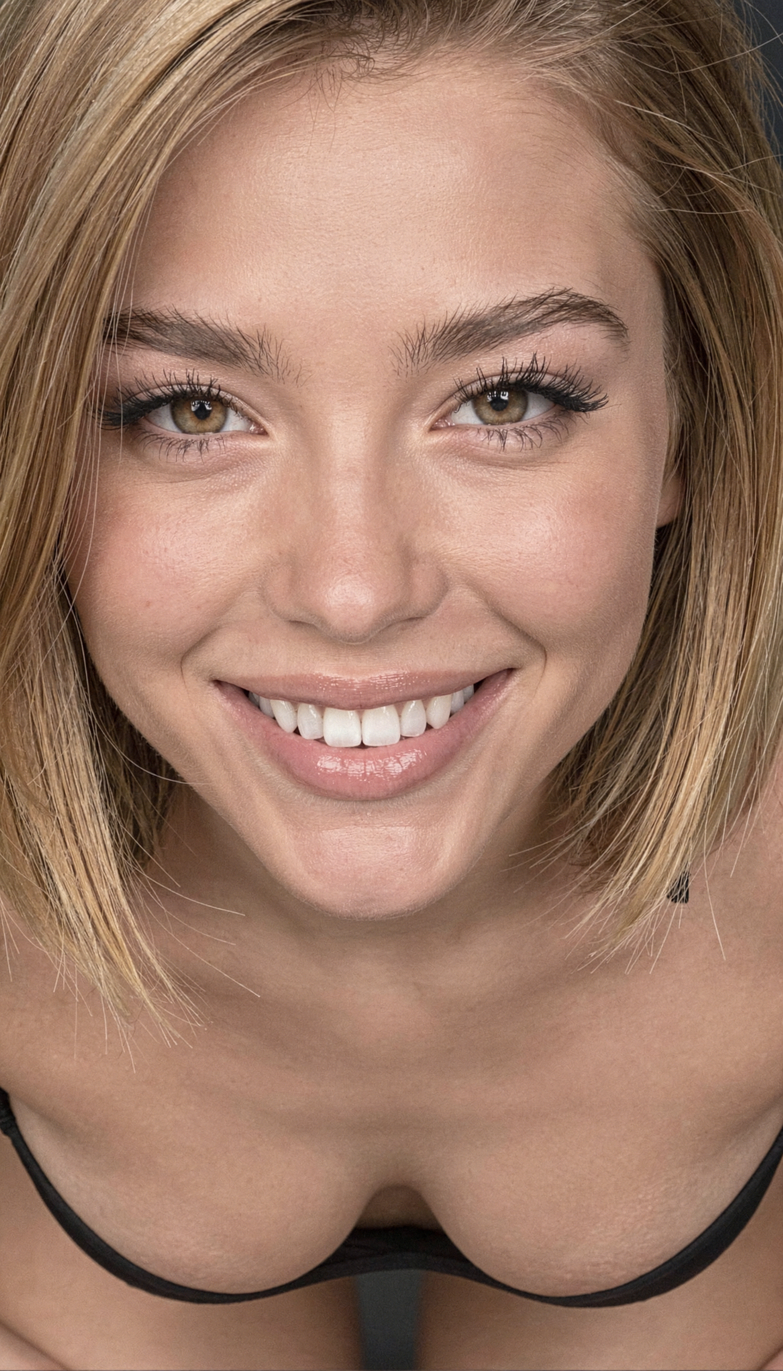 Extreme close-up high angle portrait of a person in a black garment, with soft lighting highlighting their warm hazel eyes and genuine smile.