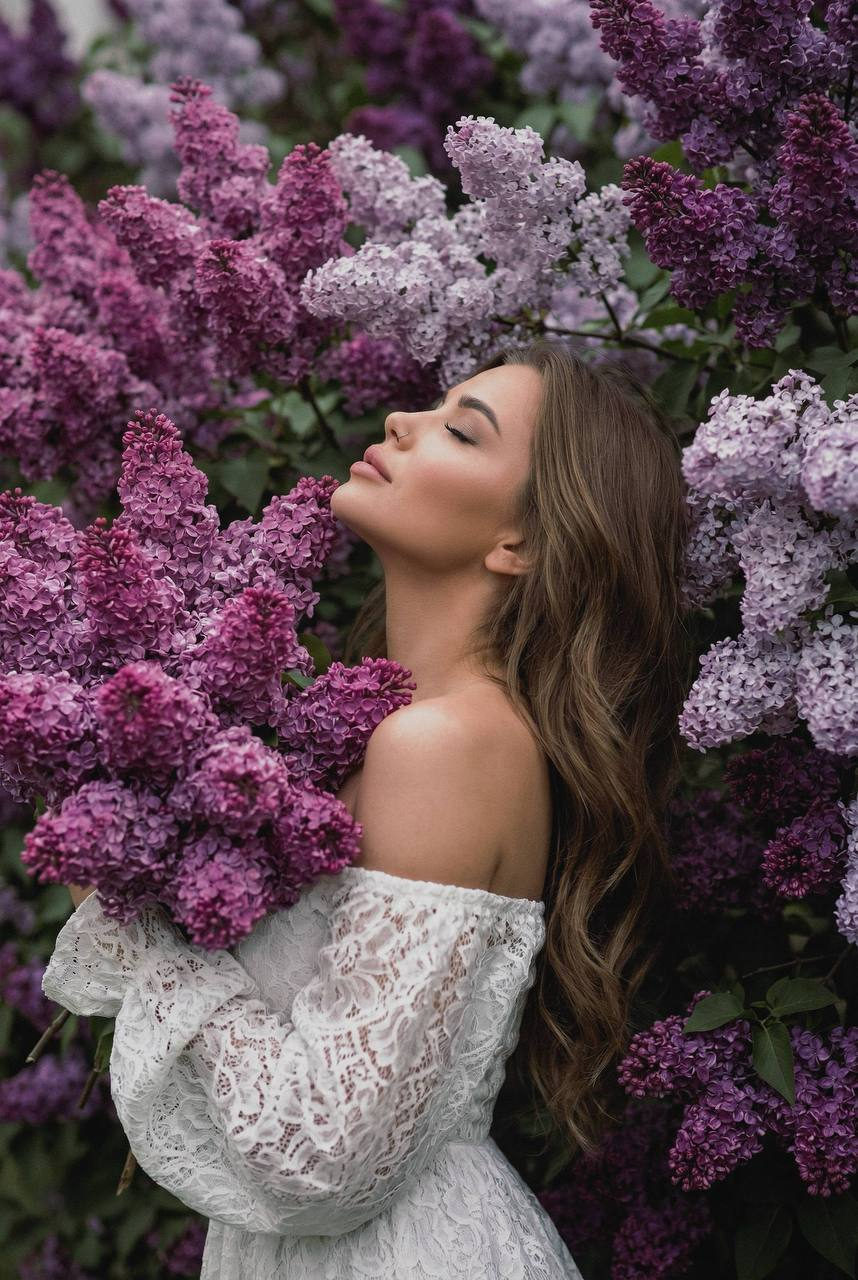 Female subject in profile wearing a white lace dress against thick lilac flowers, embodying peaceful contemplation.