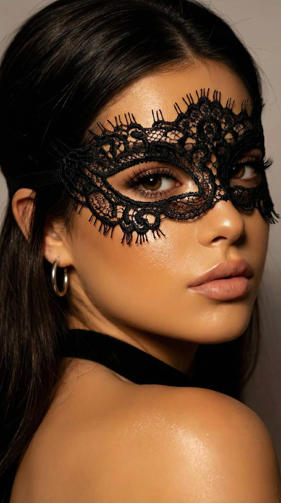 Close-up portrait of a person in a lace masquerade mask, softly illuminated with highlights and deep shadows, showing dewy skin and elegant hairstyle.