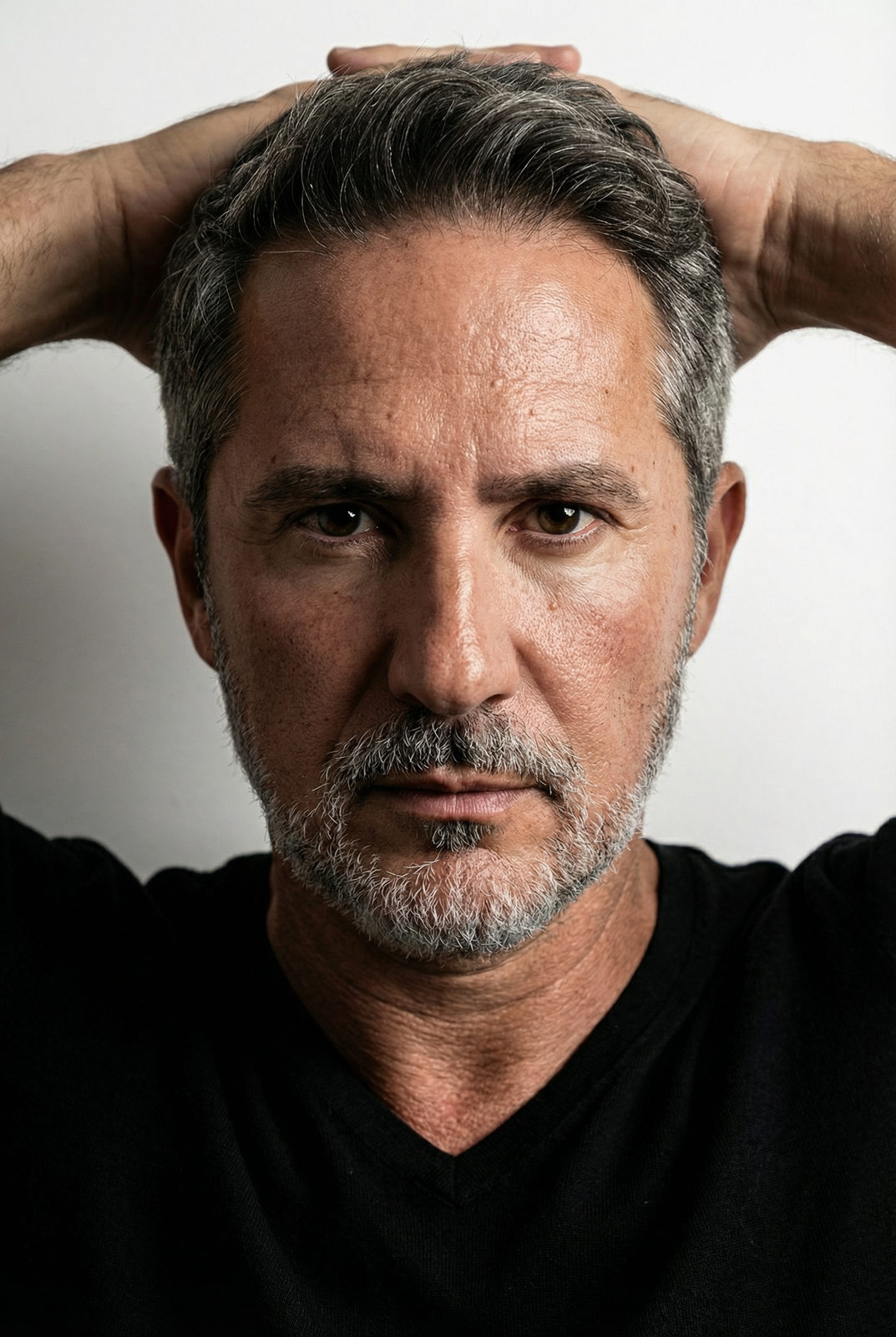 Elegant editorial portrait of a man with salt-and-pepper hair, showcasing refined grooming and a polished appearance in soft lighting.
