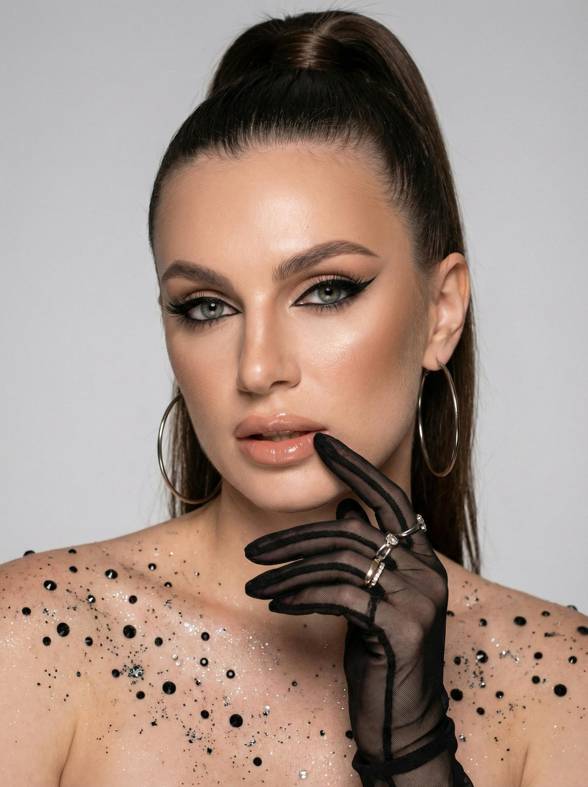 Close-up of a model with rhinestones, glossy lips, and bold makeup.