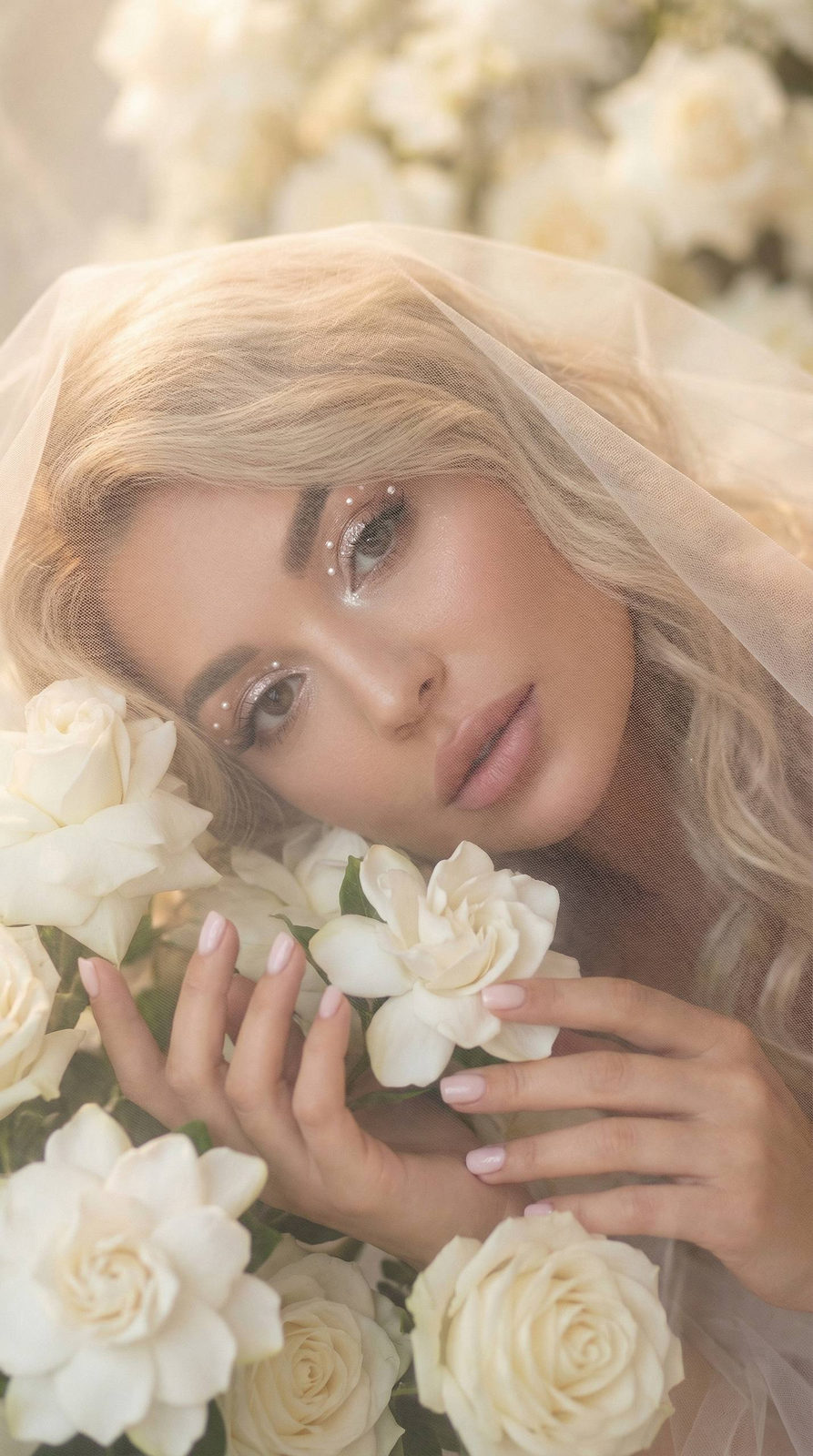 A serene woman with a soft veil amidst white flowers, her flowing hair creating gentle waves.