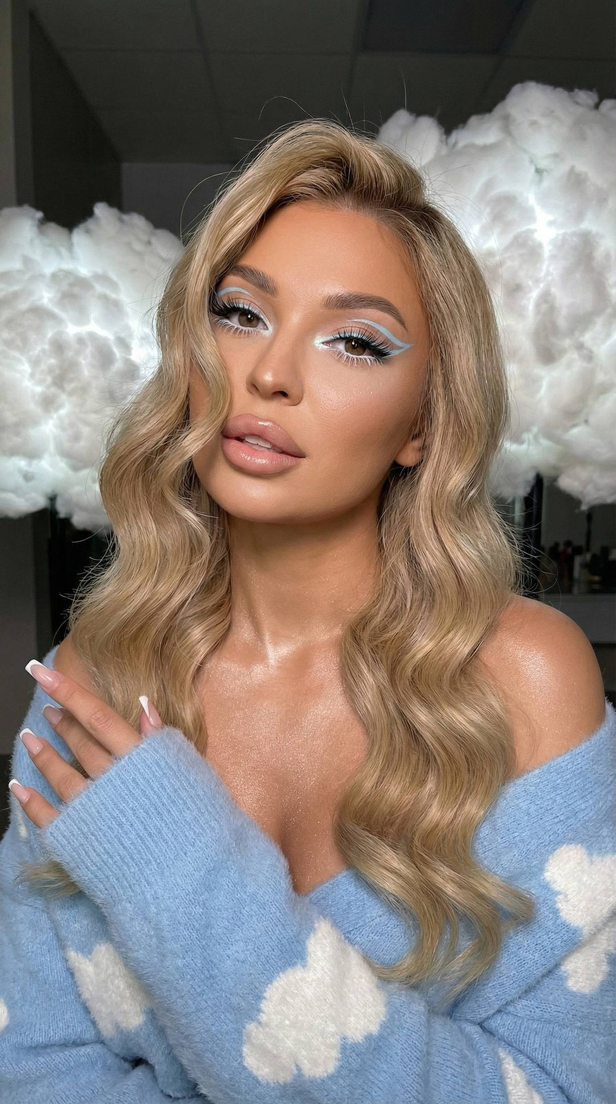 Close-up of a girl in a high fashion style with long glossy hair, elegant makeup, and beachy waves, against fluffy clouds.
