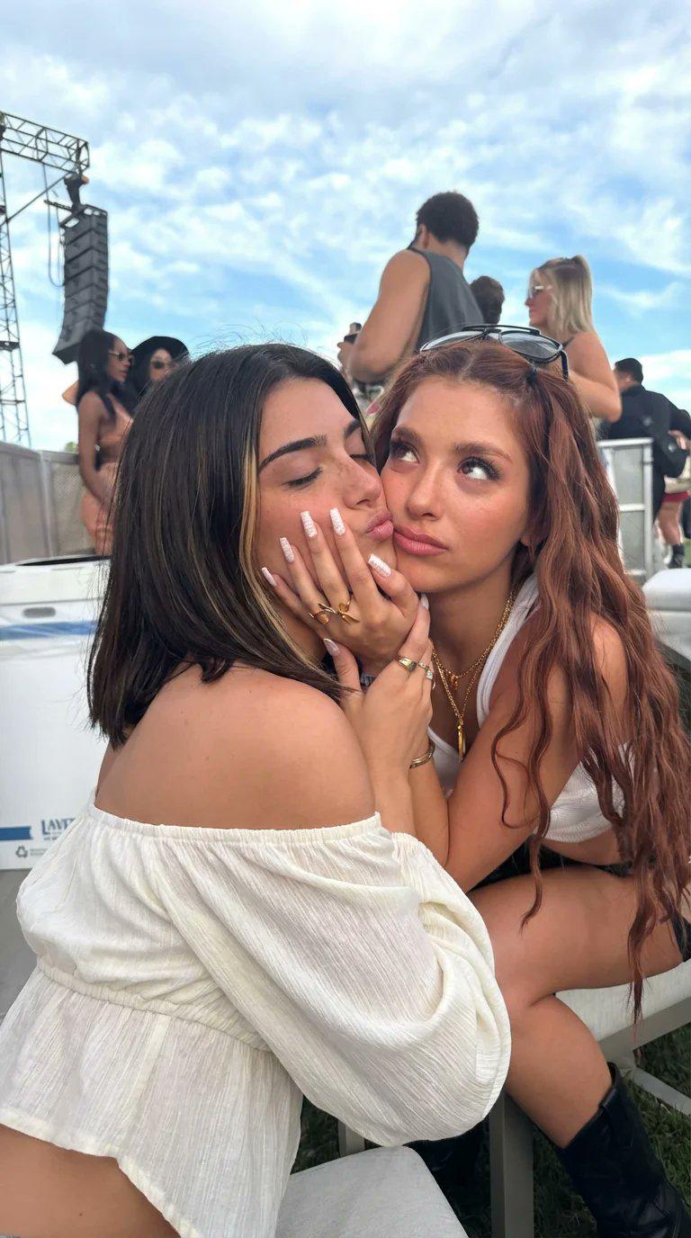 Two women at a festival share a cheek kiss, showcasing natural lighting and vibrant colors.