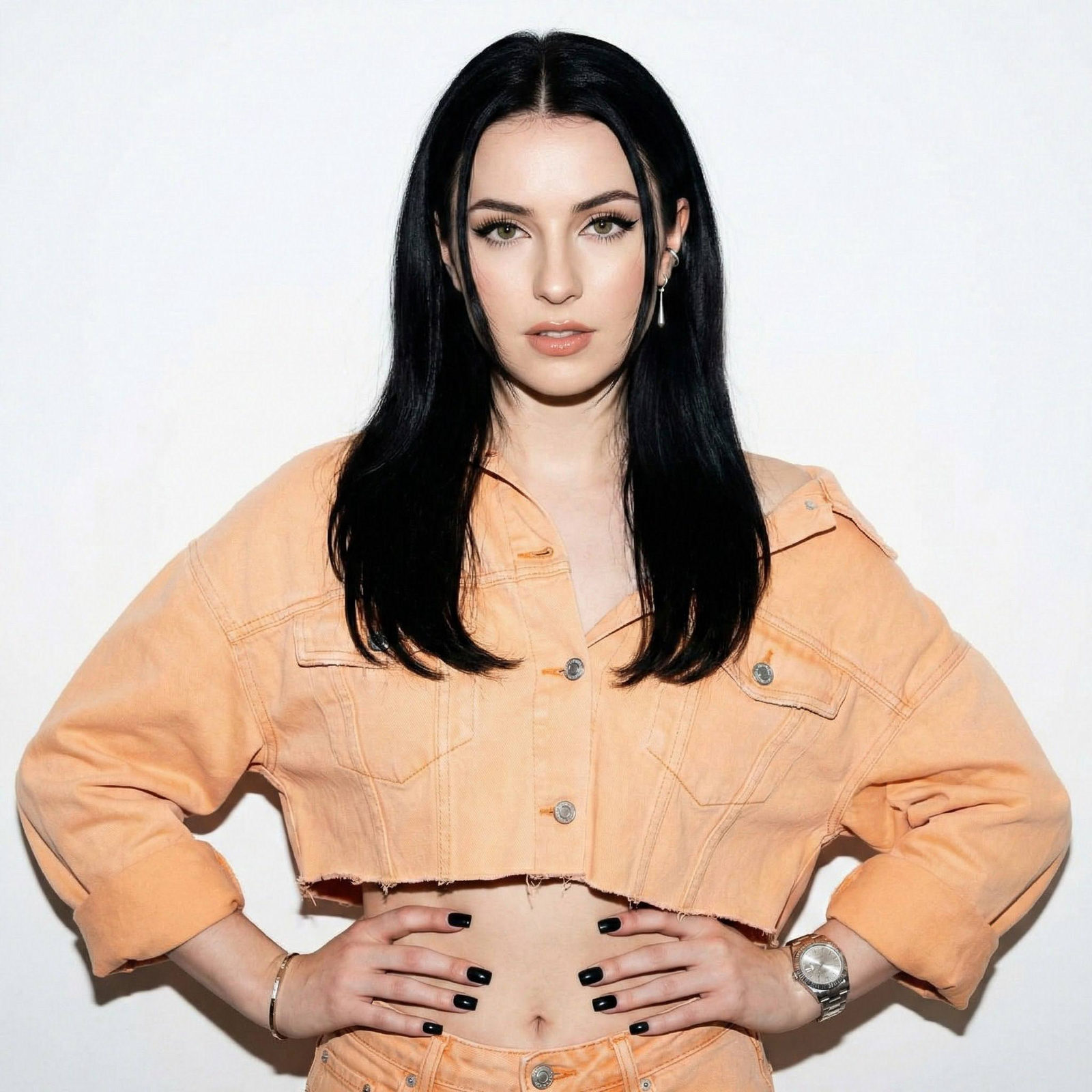 A confident young woman with a playful gaze, against a white wall. Captured in a light orange oversized denim jacket, exuding charisma.