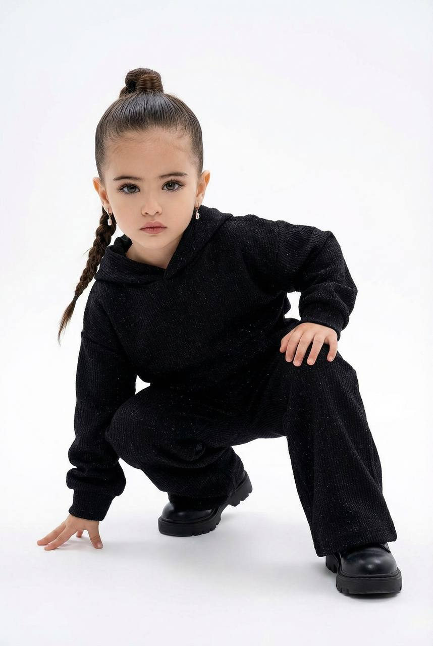 Child in a crouched pose wearing a textured two-piece outfit with a high bun hairstyle in a clean studio background.
