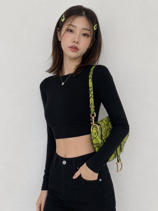 A studio portrait of a woman wearing a tight black cropped top and high-waisted jeans, holding a snakeskin shoulder bag.