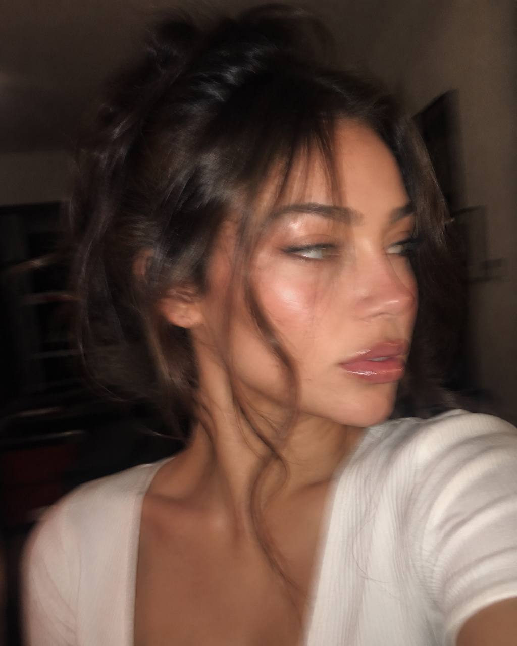 Close-up portrait of a person with warm side lighting, featuring soft shadows and natural contours in a blurred dark interior.