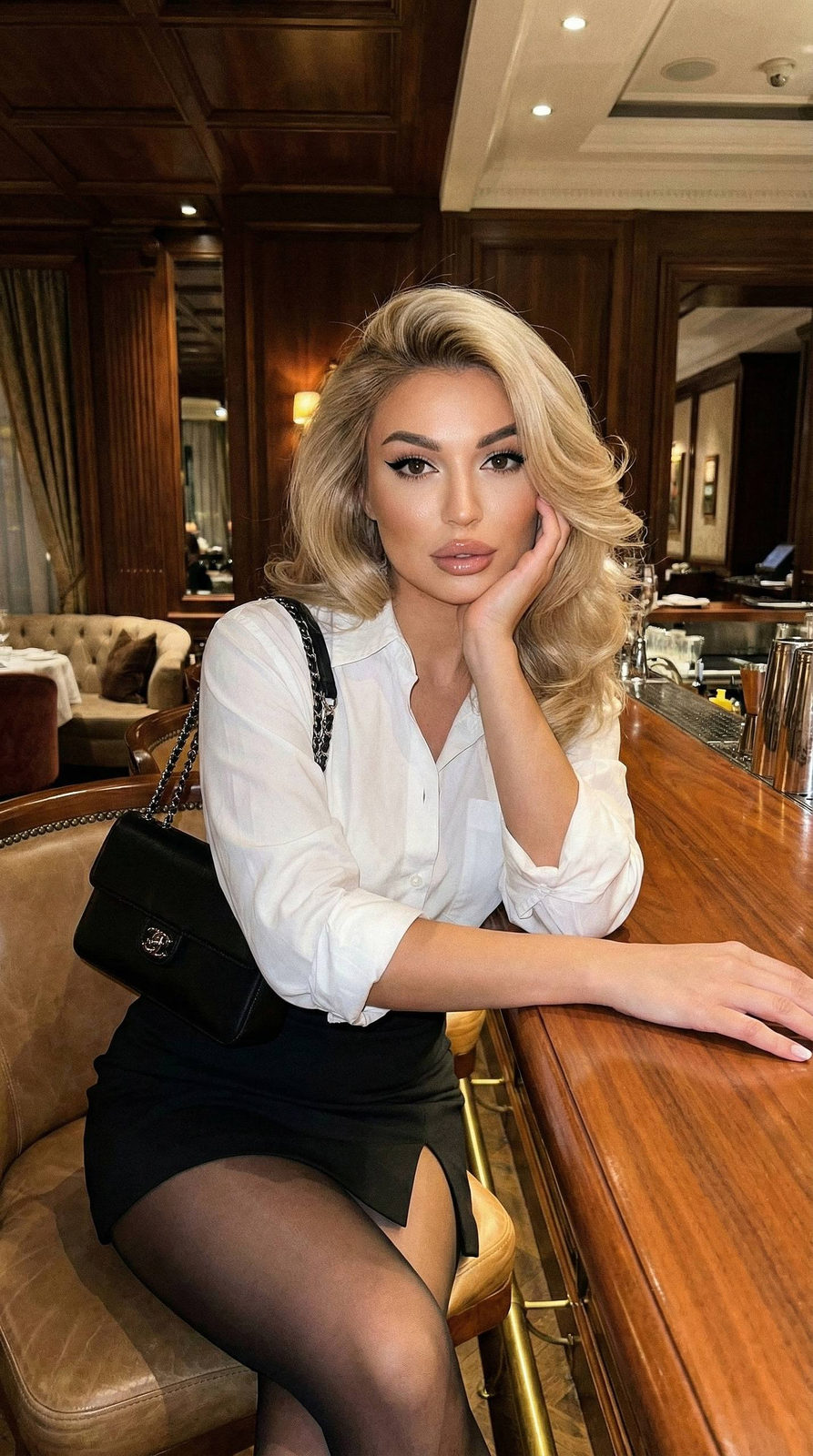 Close-up of a girl at a wooden bar with evening makeup, stylish attire, and glossy lips.