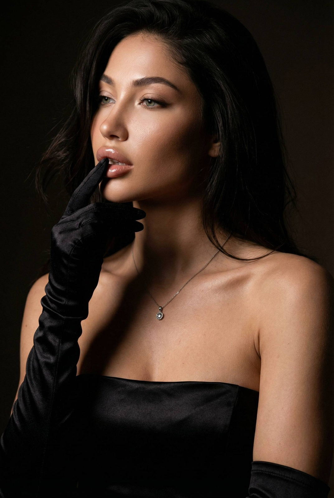 Close-up dark luxury fashion portrait of a woman with gloved hand touching her lips, soft shadows enhancing the elegant composition.