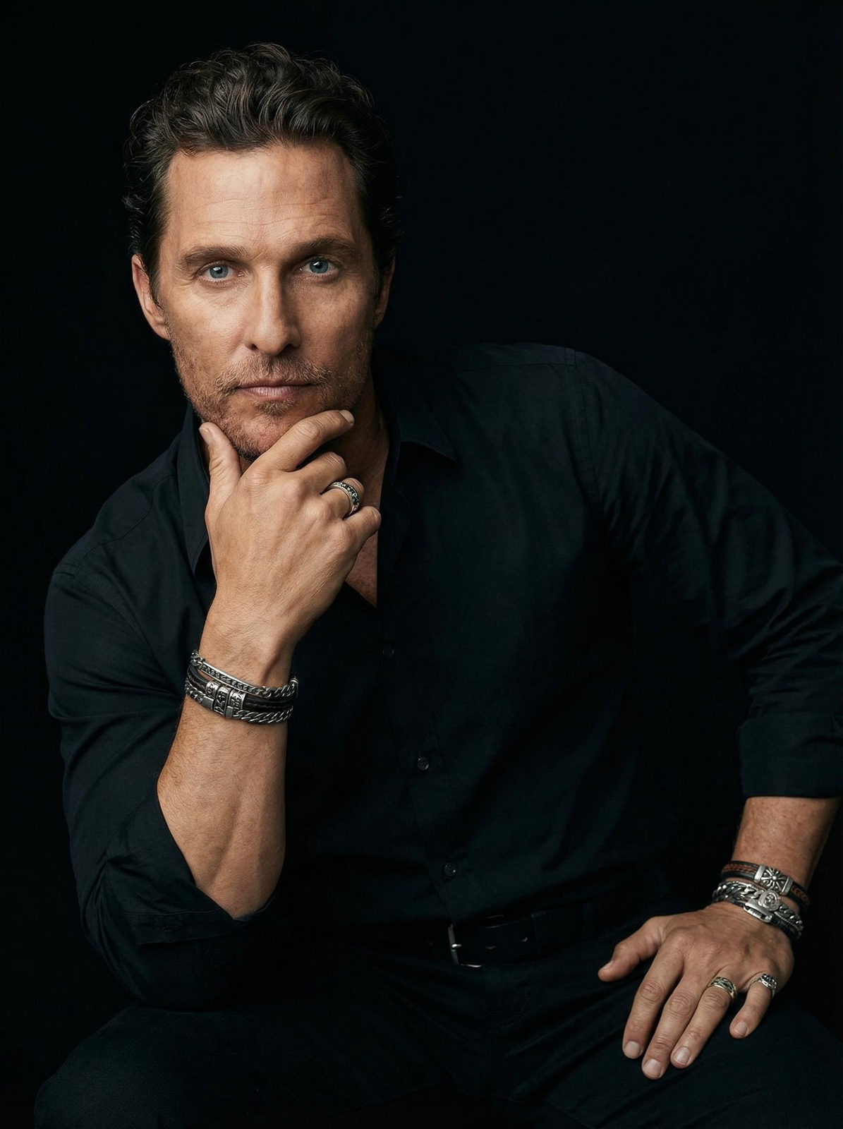 A man reclining with his hand on his chin, showcasing jewelry against a softly lit background.