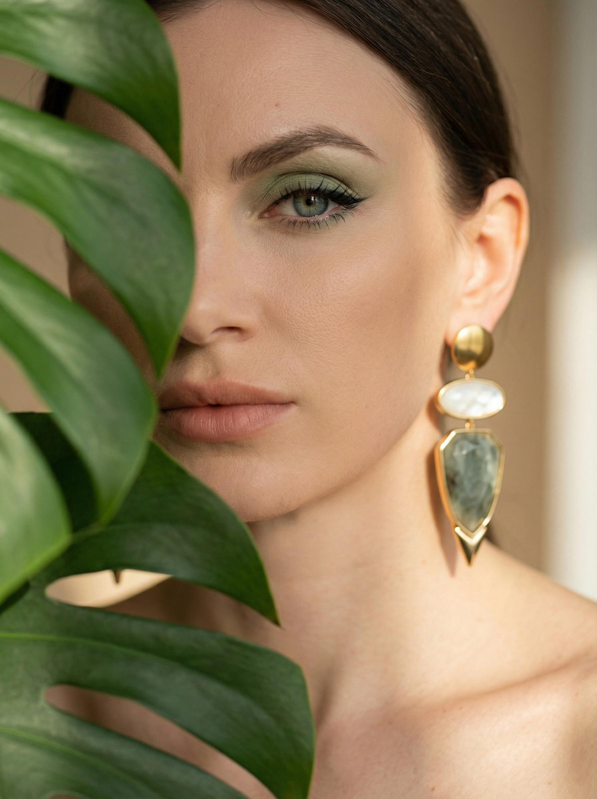 Detailed close-up portrait of a woman with a large geometric earring, soft green eyeshadow, and elegant lighting.