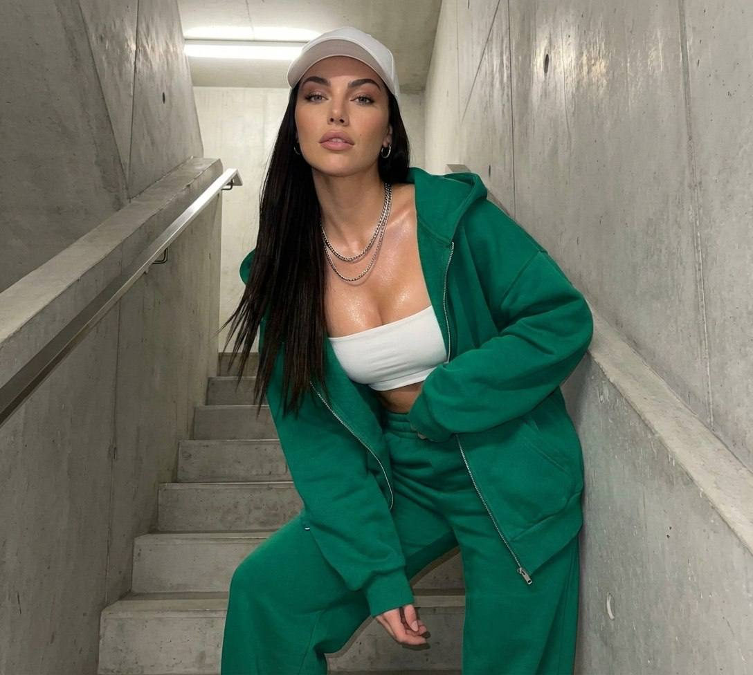 Ultra-detailed portrait of a girl in an emerald hoodie on concrete stairs, leaning confidently near the railing.