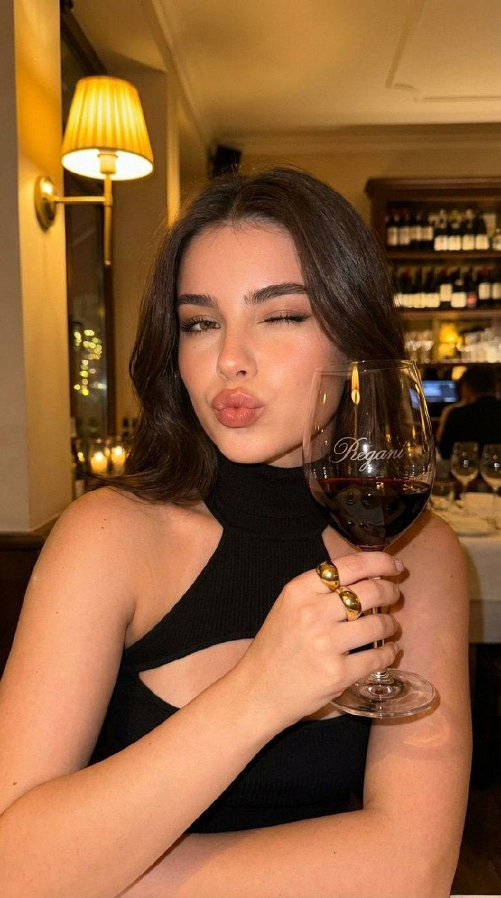 Ultra-realistic portrait of a young woman in a cozy restaurant, holding a wine glass, warm evening lighting, soft focus background.