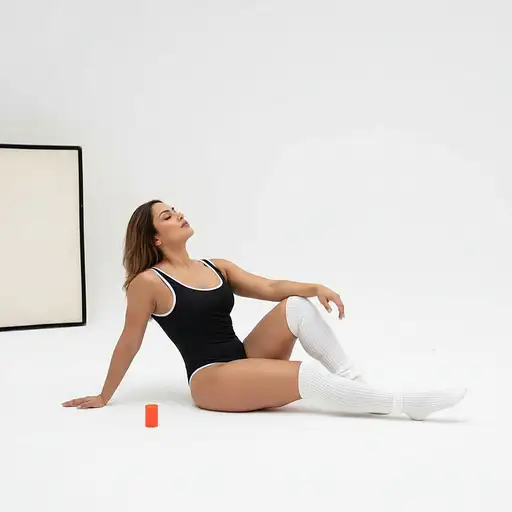 A stunning muscular curvy woman with long light brown hair poses gracefully in a minimalist studio wearing a black swimsuit.