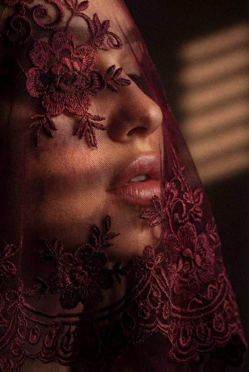 An ultra-realistic fashion portrait featuring a face partially covered by sheer crimson lace fabric, highlighting skin texture.