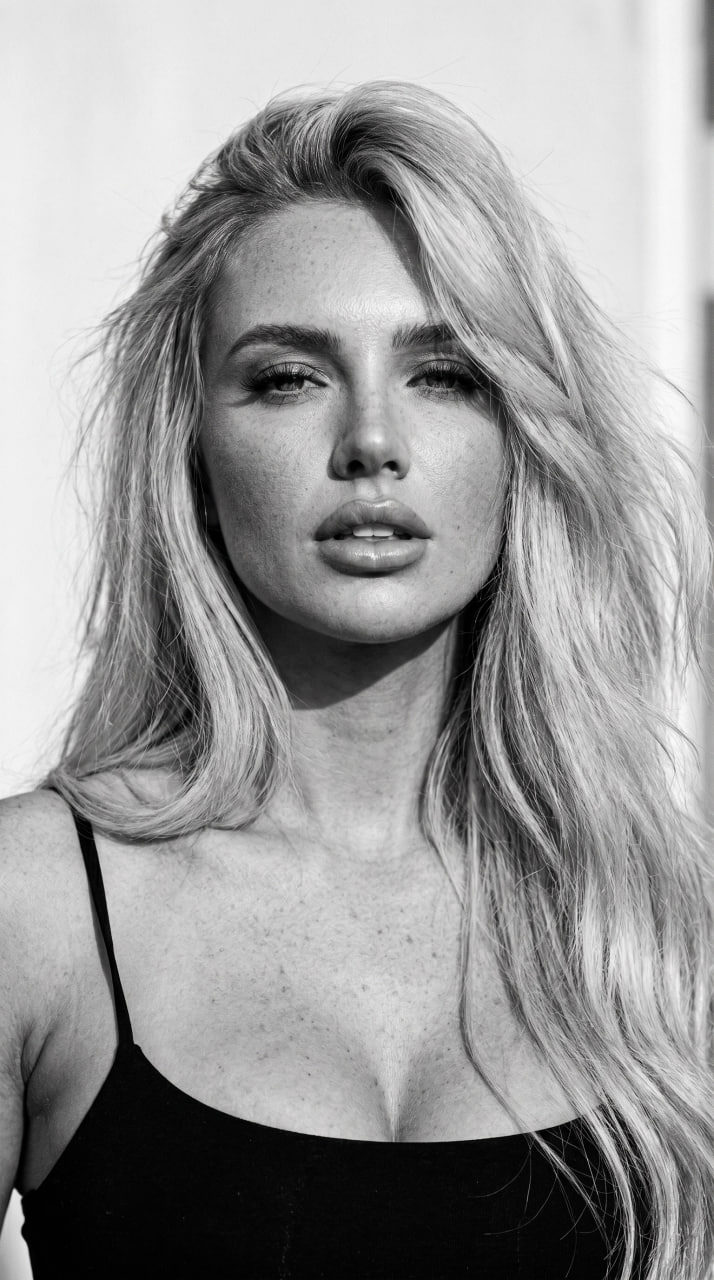 A girl with windswept hair in a black top gazing at the camera, captured in a high-contrast monochrome style.