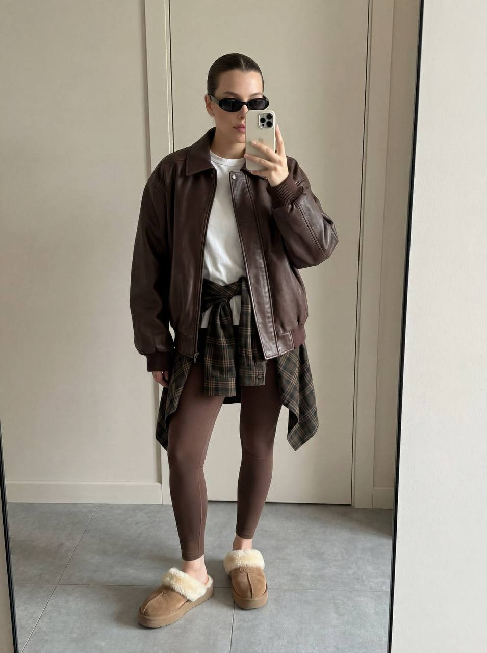 Full-length mirror selfie of a young woman in chocolate layered fashion, sporting an oversized bomber jacket, plaid shirt, and cozy mules.