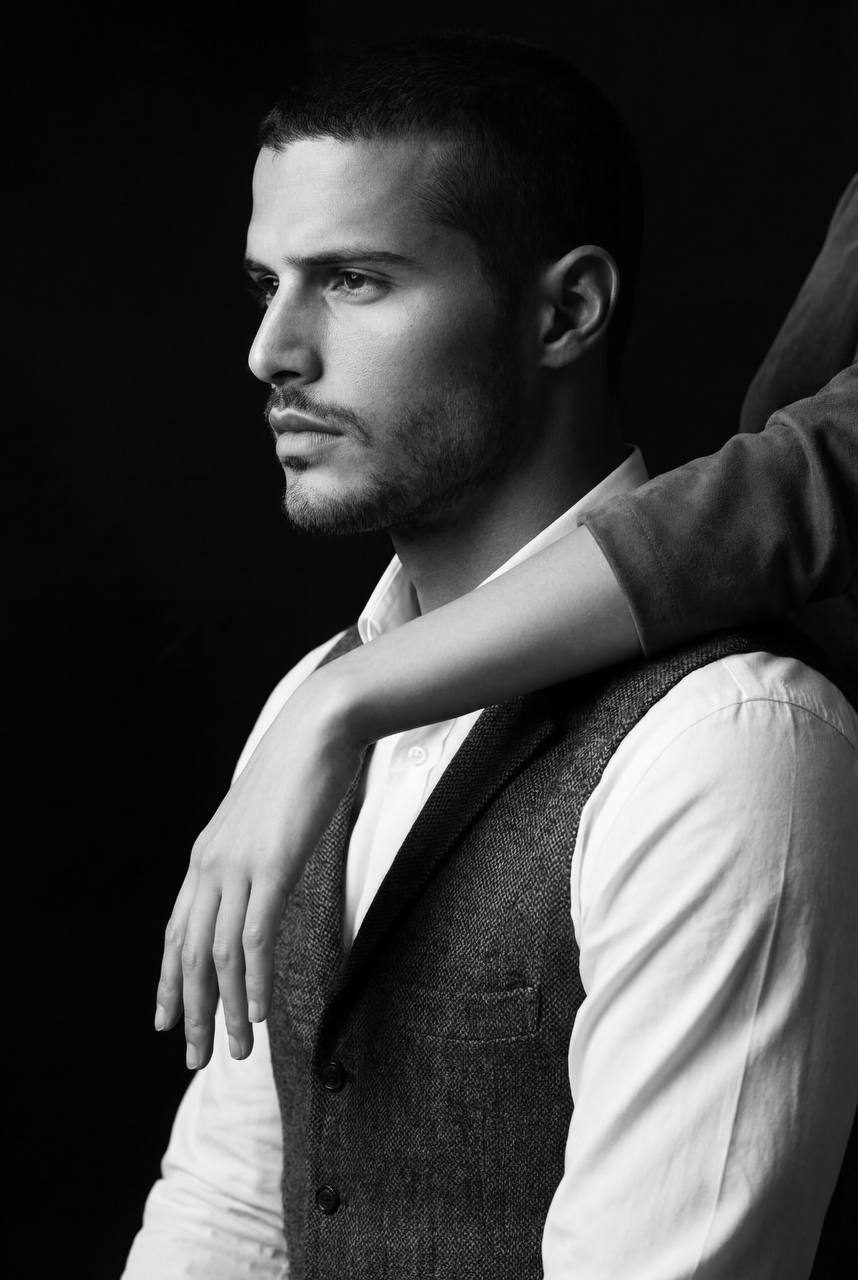 A man in profile, wearing a classic shirt and dark vest, gazes seriously into the distance with a calm posture.