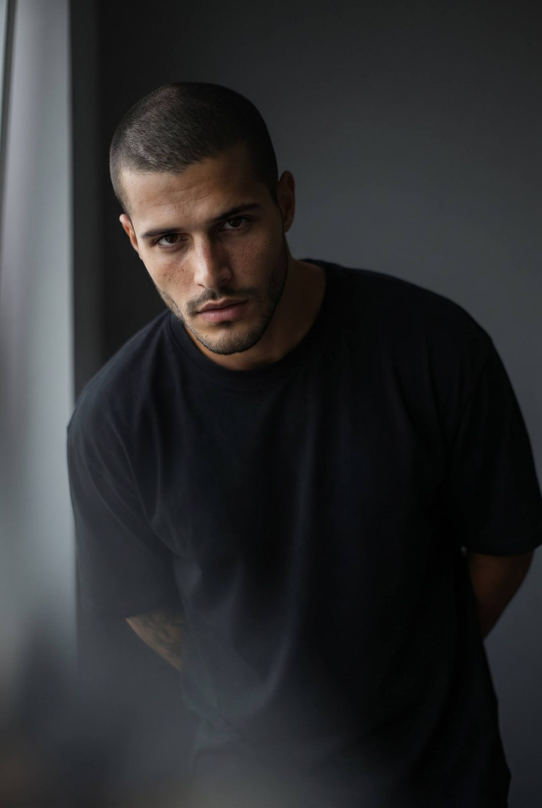 Cinematic portrait of a man indoors with dramatic gaze, leaning slightly forward and captured with soft window light.