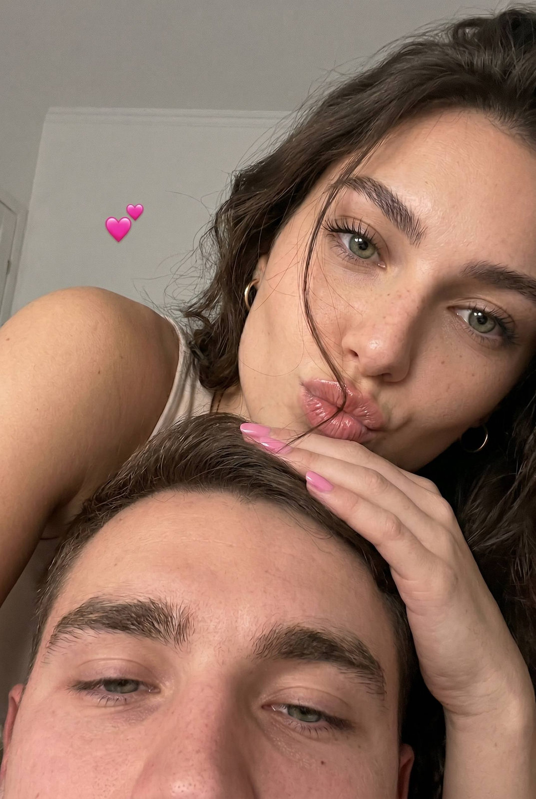 A close-up selfie of two young adults with soft lighting, their faces close together and playful mood, accentuating their intimacy.