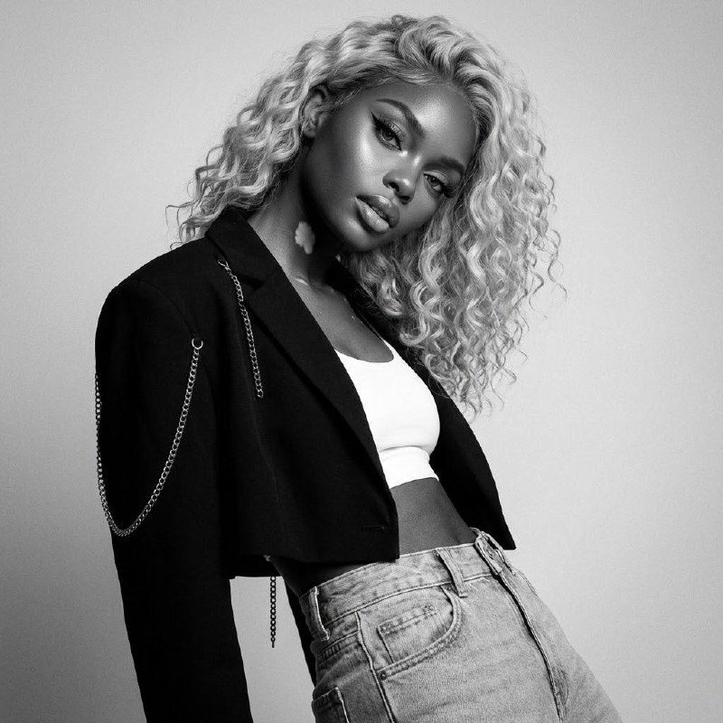A hyper-realistic fashion portrait of a model in an oversized jacket with chains, shot in monochrome. The model tilts her head with parted lips.