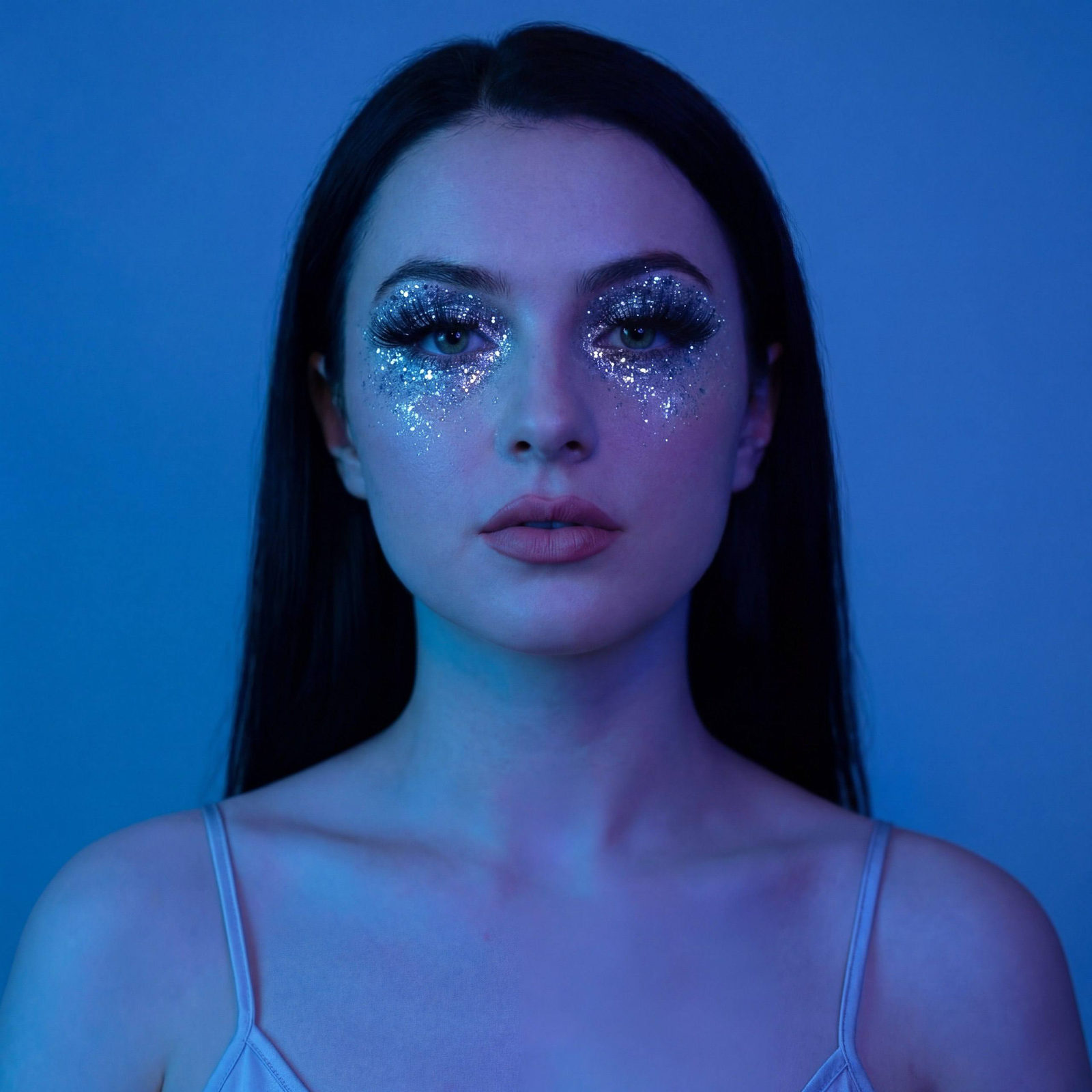 A girl with long straight hair gazes into the camera, showcasing silver glitter eye makeup that resembles a starry sky.