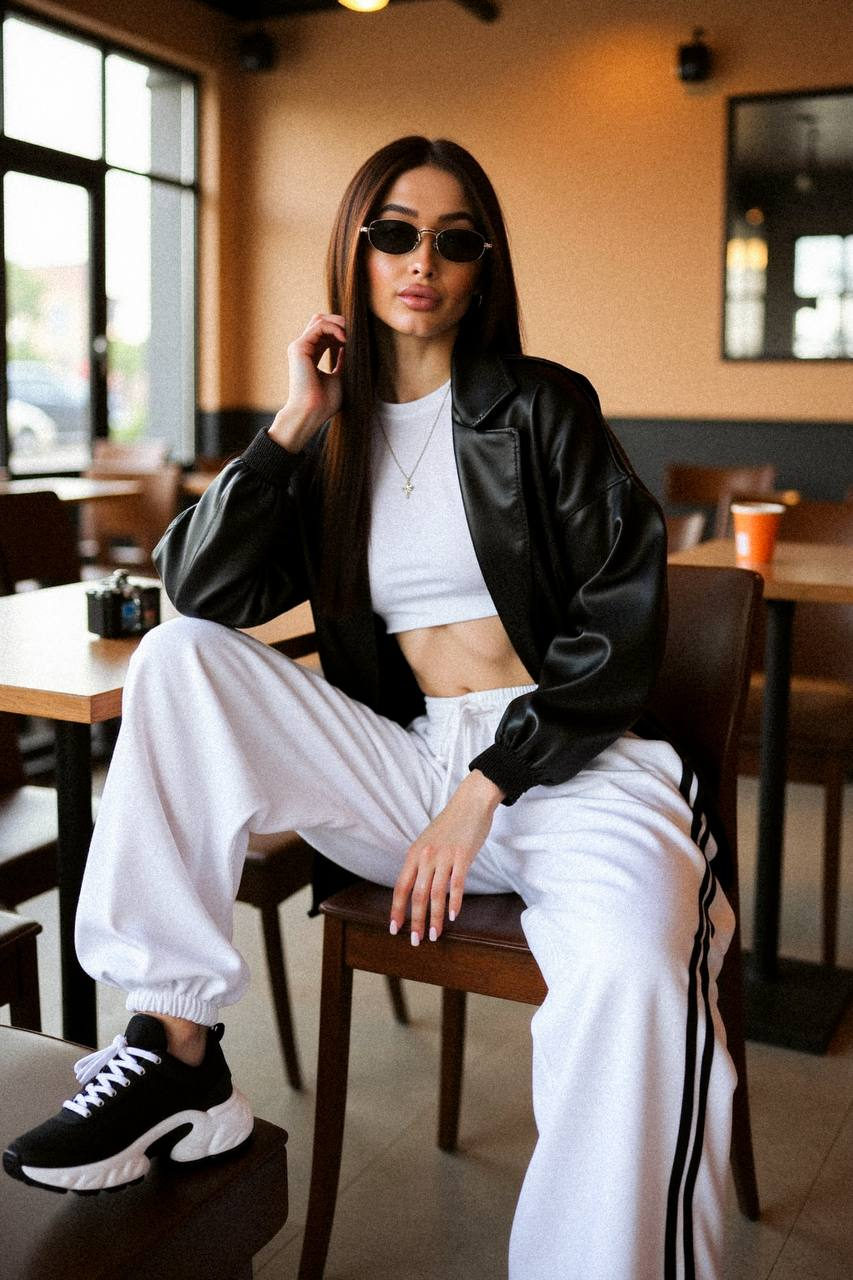 A stylish woman in a modern café, wearing a cropped sports top, oversized sweatpants, and futuristic sunglasses, with warm earthy tones around her.