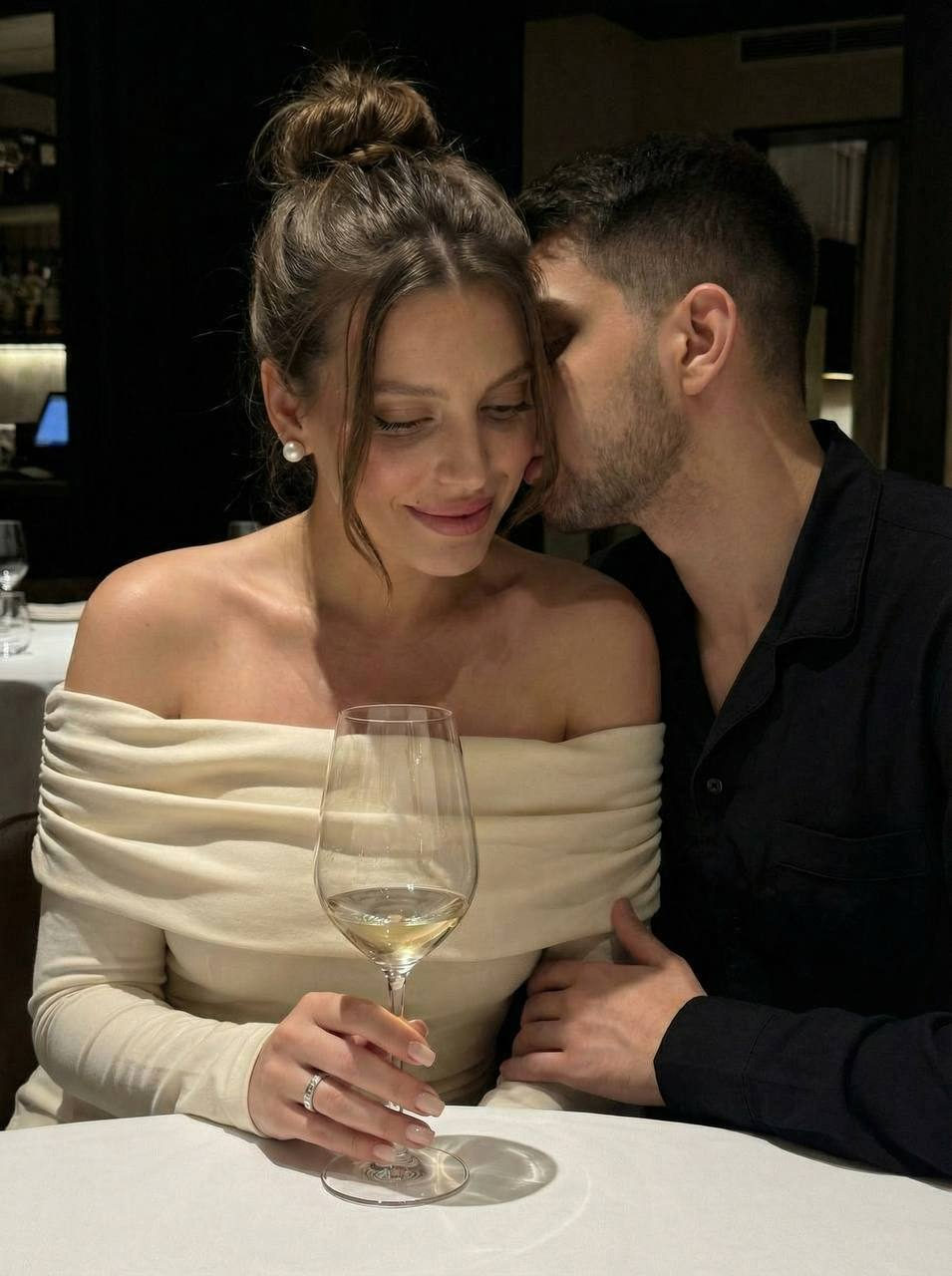 Couple sharing a tender moment at a dimly lit dinner table, warm shadows, elegant wine glass near them.