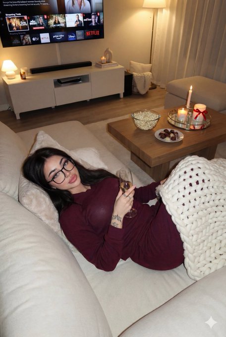 A woman in a cozy living room, lying on a sectional sofa with soft warm candlelight illuminating the space.