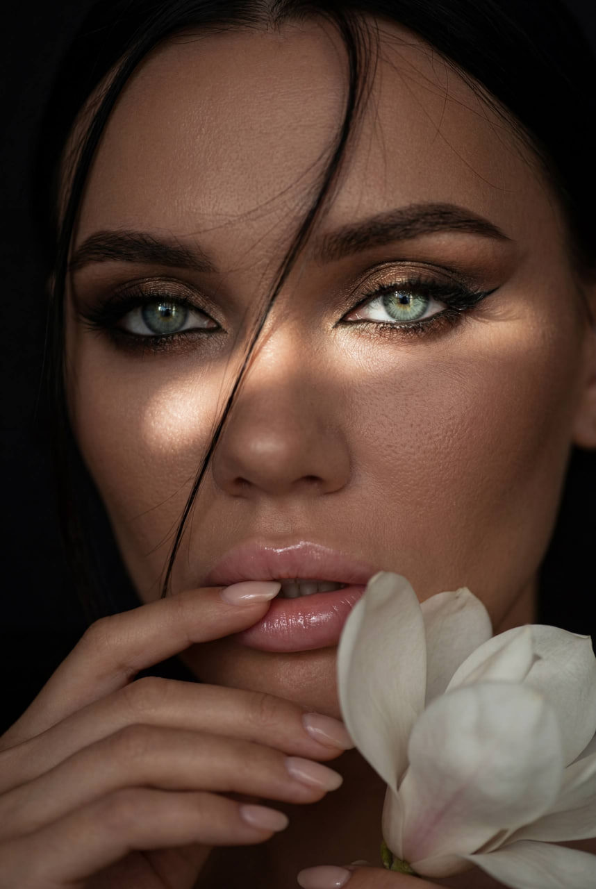 Close-up of a woman's face with green eyes, natural glow, and a white magnolia.