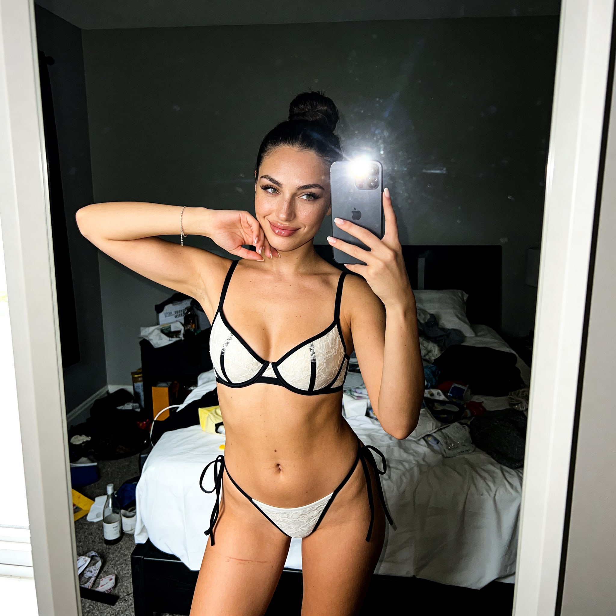 A realistic bedroom selfie of Lily in skimpy underwear, showcasing a messy background and a cute smile.
