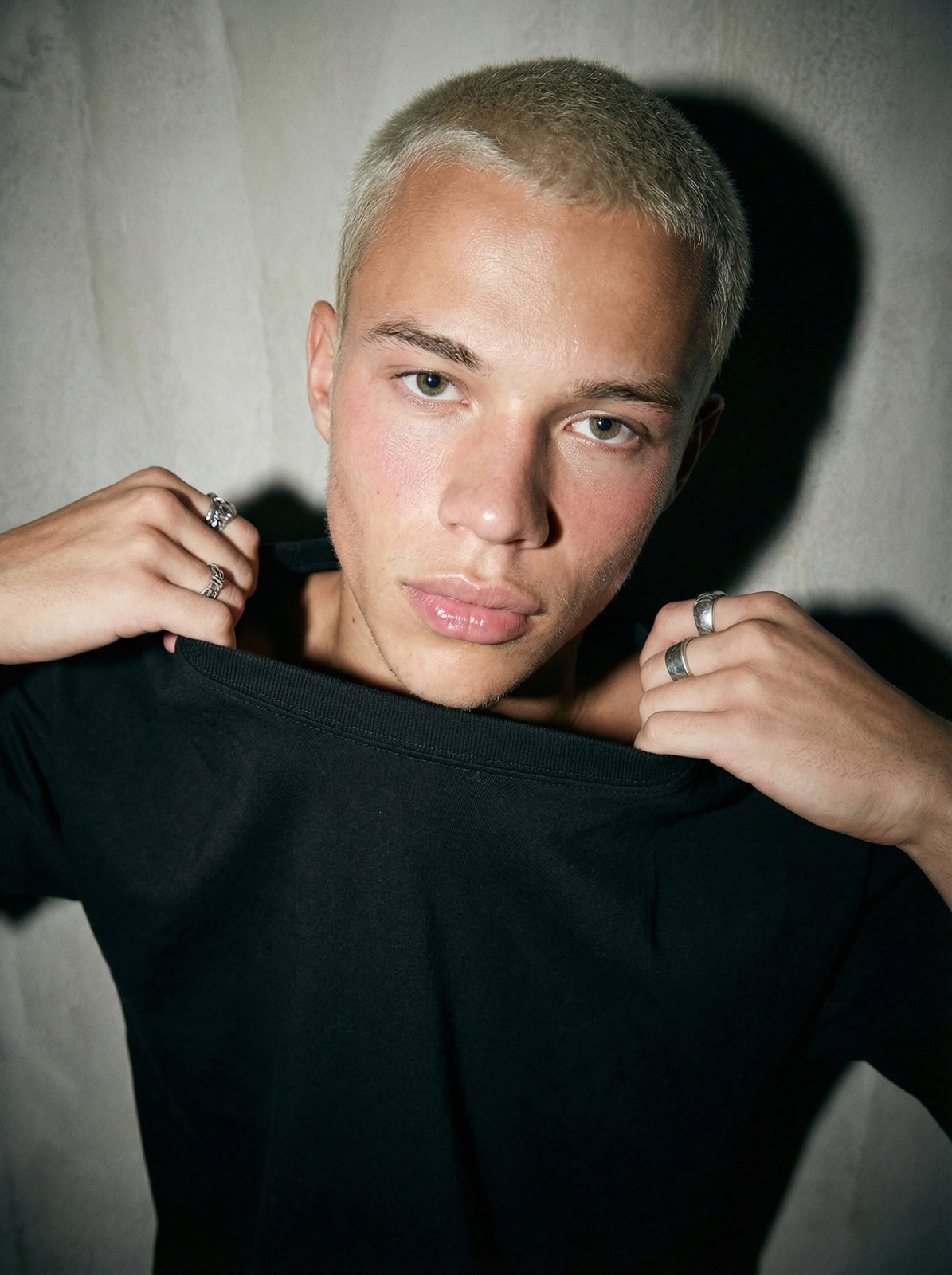 Close-up of a young man pulling a shirt in front of him against a concrete wall, showcasing natural skin texture and deep shadows.