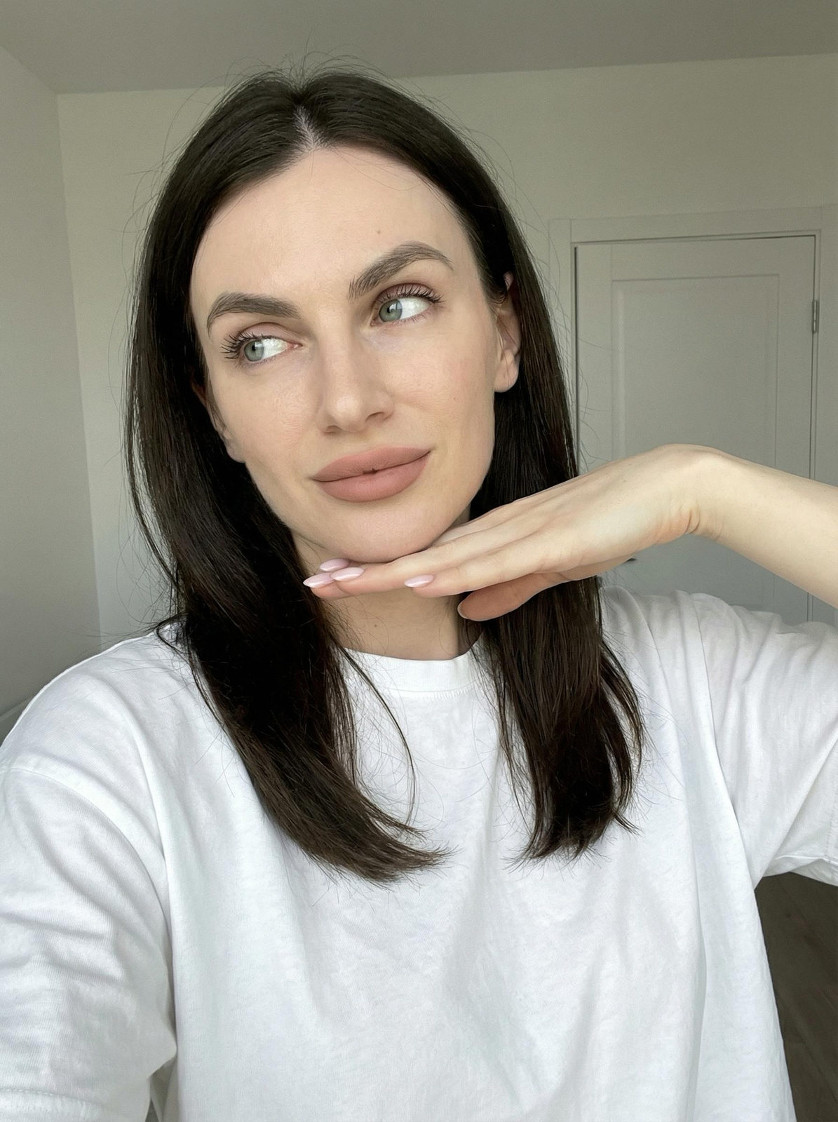 A woman with playful pose, light makeup, and casual oversized T-shirt, softly illuminated by natural light.