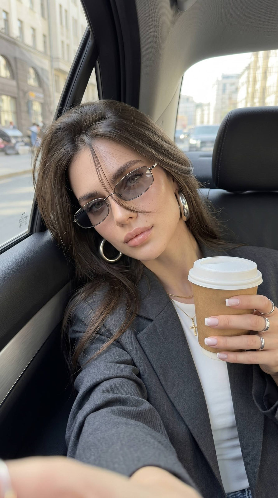 A girl in a car backseat taking a selfie, natural perspective with long dark hair, stylish sunglasses, relaxed expression.