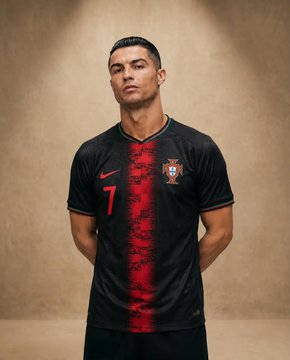 A professional athlete in a black Portugal soccer jersey against a muted beige backdrop, soft lighting highlights his composed expression.