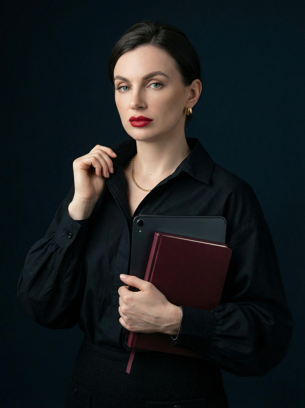 A woman in a dark studio, wearing a textured blouse and holding a diary and tablet, showcasing soft editorials lighting.