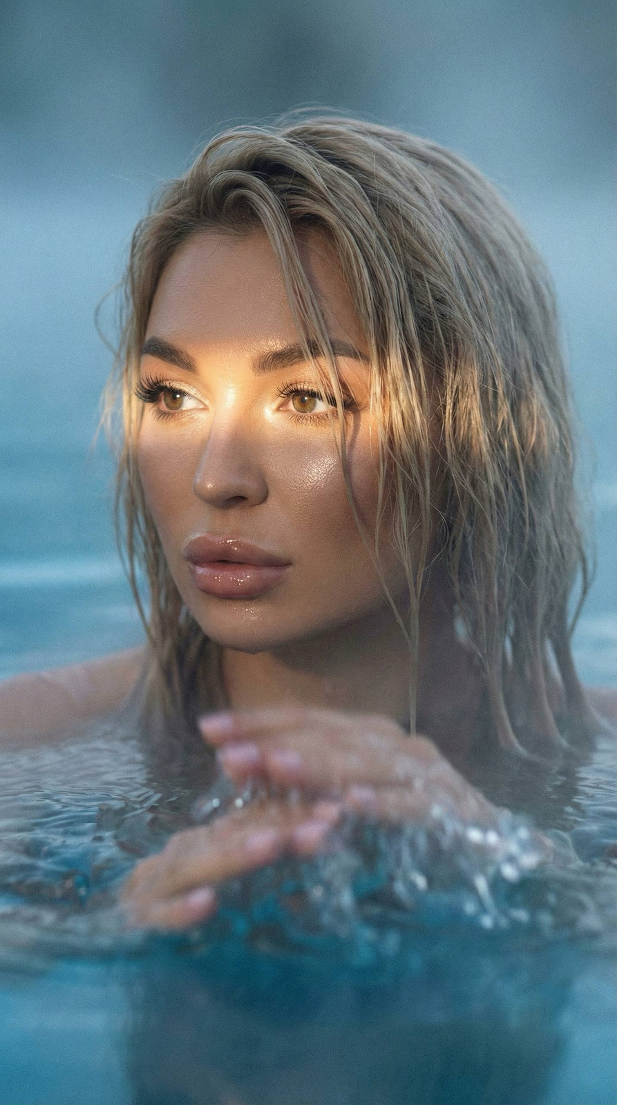 Close-up portrait of a woman in a misty lake, sunlight highlights her features and wet hair, creating a serene atmosphere.