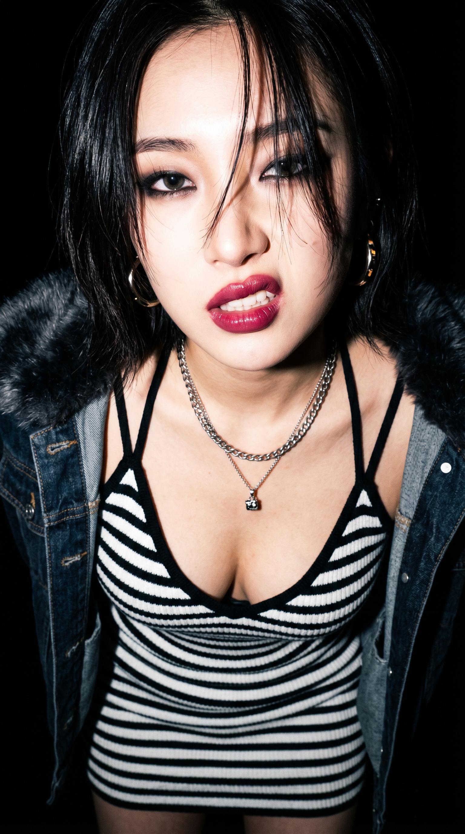 Close-up of a model in a striped minidress and denim jacket with dramatic lighting against a black background.