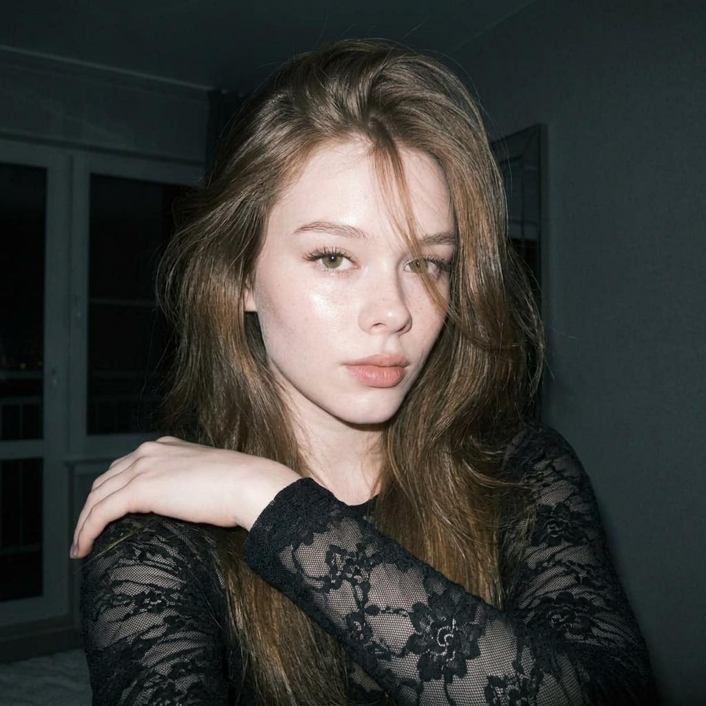 A medium close-up portrait of a woman in a black lace top with soft natural volume hair and cityscape in the blurred background.