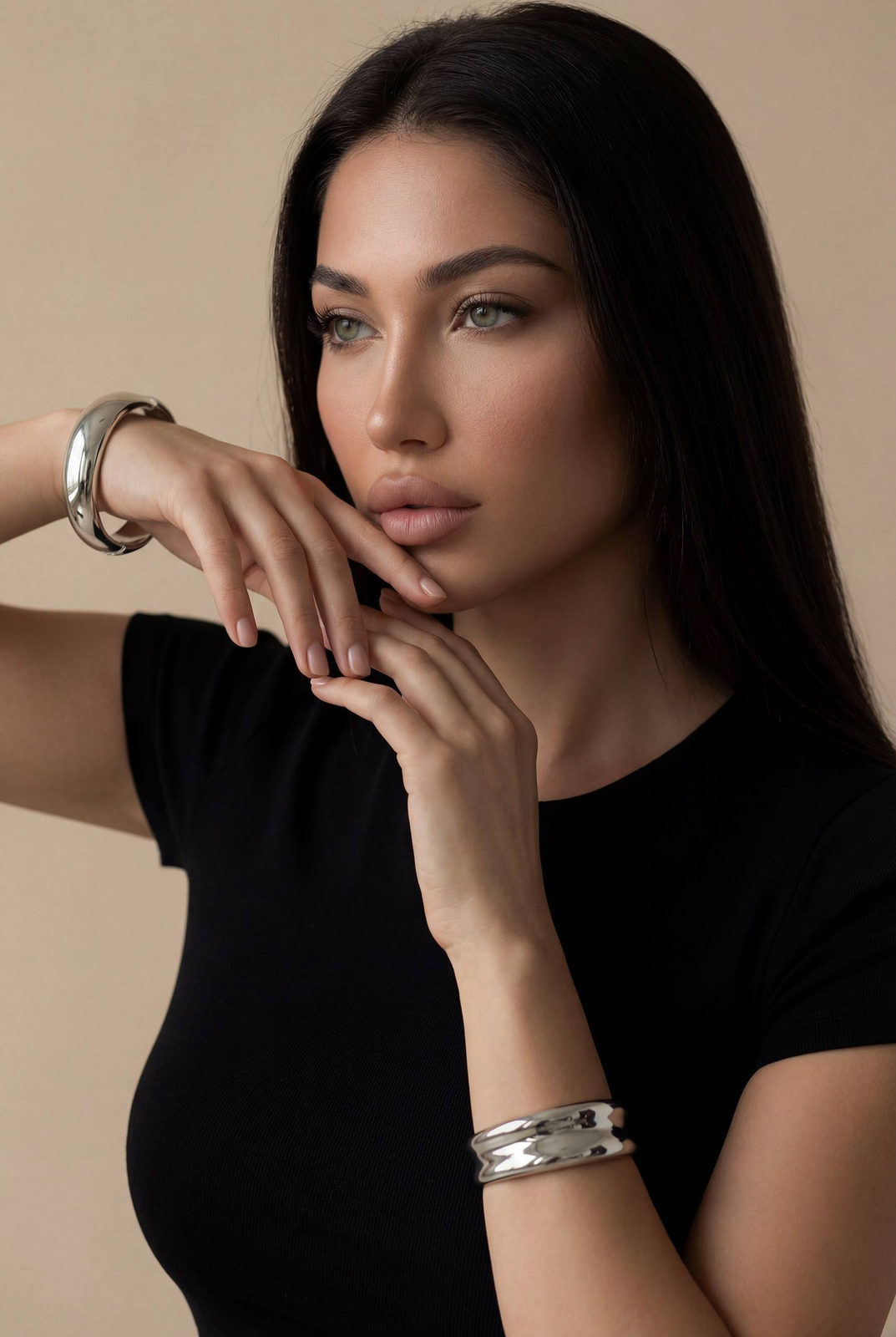 A calm editorial portrait of a woman in a minimalist studio with soft lighting, hands raised near her face, and a thoughtful expression.