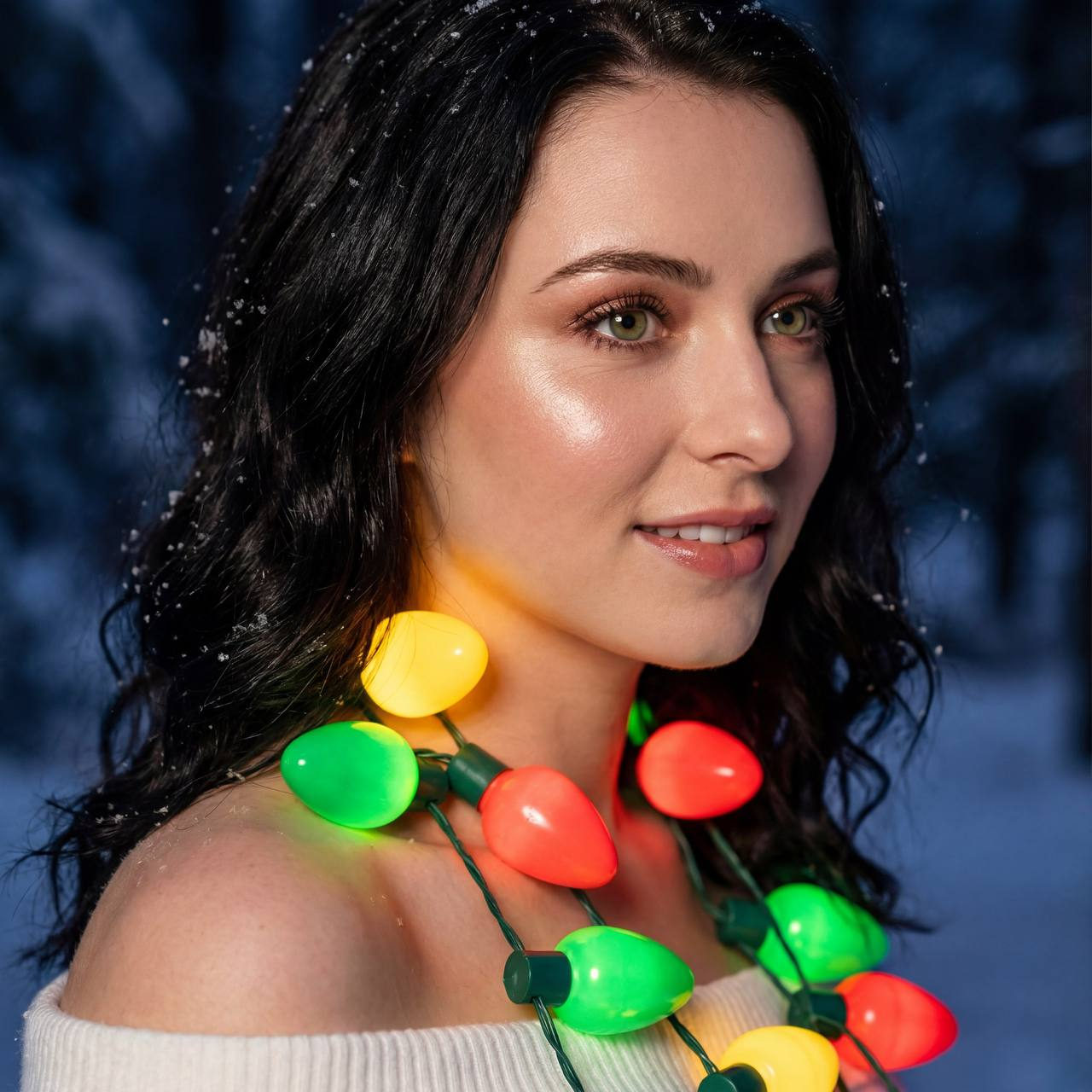 Close-up portrait of a woman with a warm sweater glowing under a garland of bright lights against a snowy night forest.
